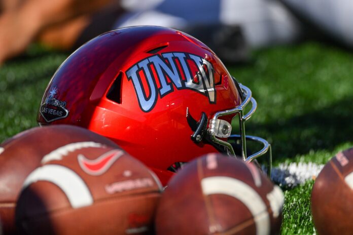 The UNLV Rebels helmet placed on the field next to a bunch of footballs.