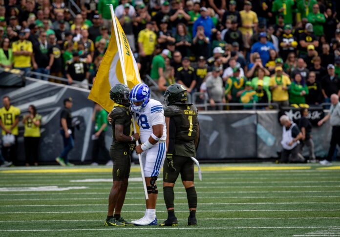 BYU offensive lineman Kingsley Suamataia hands off a flag honoring Oregon’s Spencer Webb to Oregon wide receiver Isaah Crocker before the start of a Saturday, Sept. 17, 2022, game at Autzen Stadium.