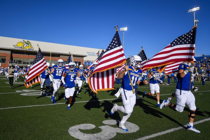 South Dakota State’s Jackrabbits football team runs on to the field with U.S. flags before the game against Missouri State.