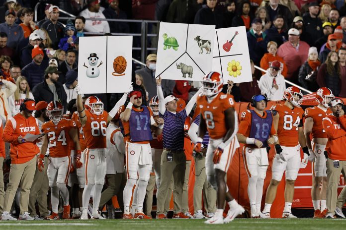 Clemson Tigers players and staff hold up cards with symbols and pictures on the sidelines to call plays during the second quarter of their game against the Boston College Eagles at Alumni Stadium.