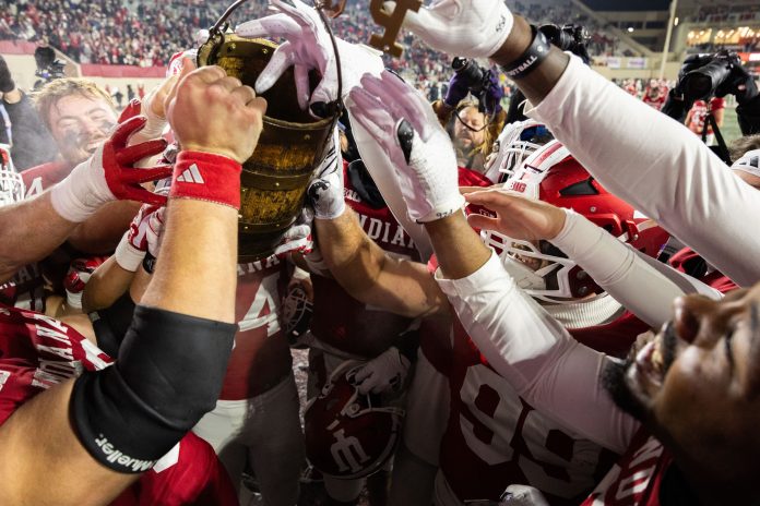 Nov 30, 2024; Bloomington, Indiana, USA; Indiana Hoosiers players celebrate with the Old Oaken Bucket after defeating Purdue Boilermakers at Memorial Stadium. Mandatory Credit: Trevor Ruszkowski-Imagn Images