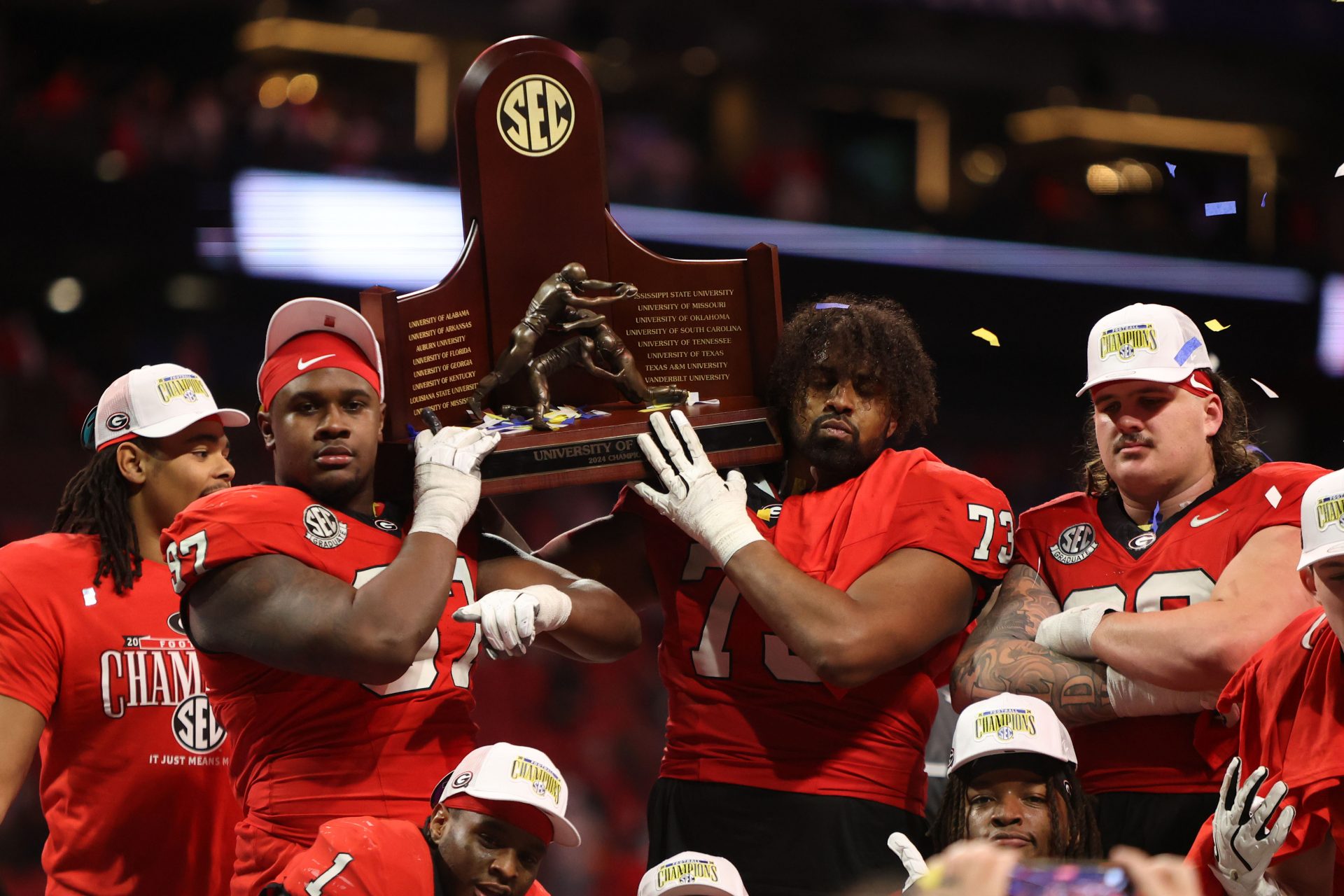 Georgia Bulldogs defensive lineman Warren Brinson (97) and offensive lineman Xavier Truss (73) celebrate with the trophy after defeating the Texas Longhorns in overtime in the 2024 SEC Championship game at Mercedes-Benz Stadium.