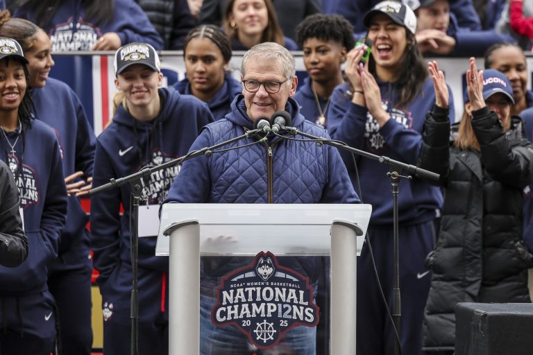 UConn Huskies head coach Geno Auriemma addresses the crowd while UConn student-athlete Paige Bueckers looks on during the Final Four champions victory parade and rally outside of the XL Center in Hartford, CT.