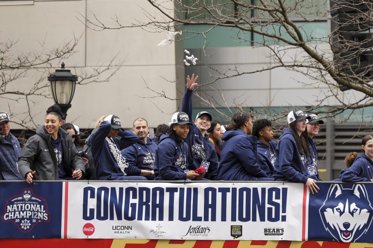 UConn student-athlete Paige Bueckers throws candy to the crowd from the bus over teammate KK Arnold during the Final Four Champions victory parade and rally outside of the XL Center in Hartford, CT.