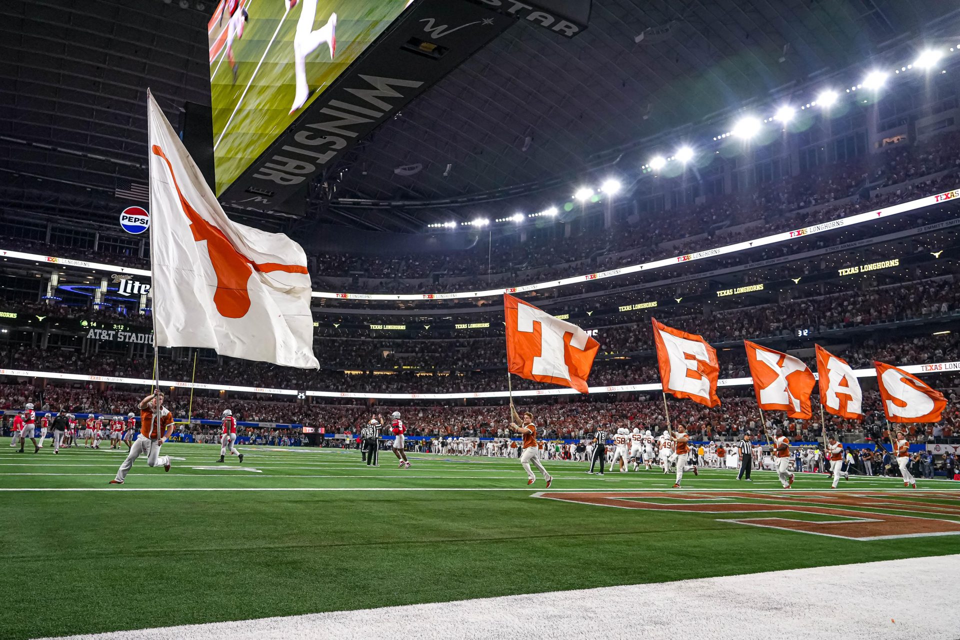 Texas Longhorns cheerleaders run flags across the field after a score during the College Football Playoff semifinal game against Ohio State in the Cotton Bowl at AT&T Stadium on Friday, Jan. 10, 2024 in Arlington, Texas.