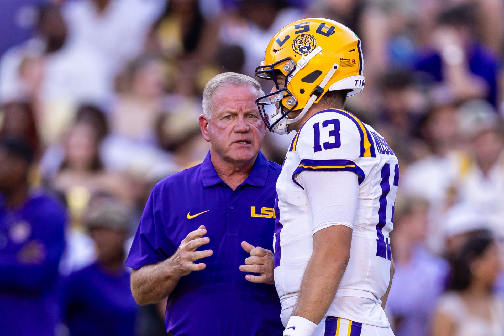LSU Tigers quarterback Garrett Nussmeier (13) talks to head coach Brian Kelly during warmups before a game against the South Alabama Jaguars at Tiger Stadium.