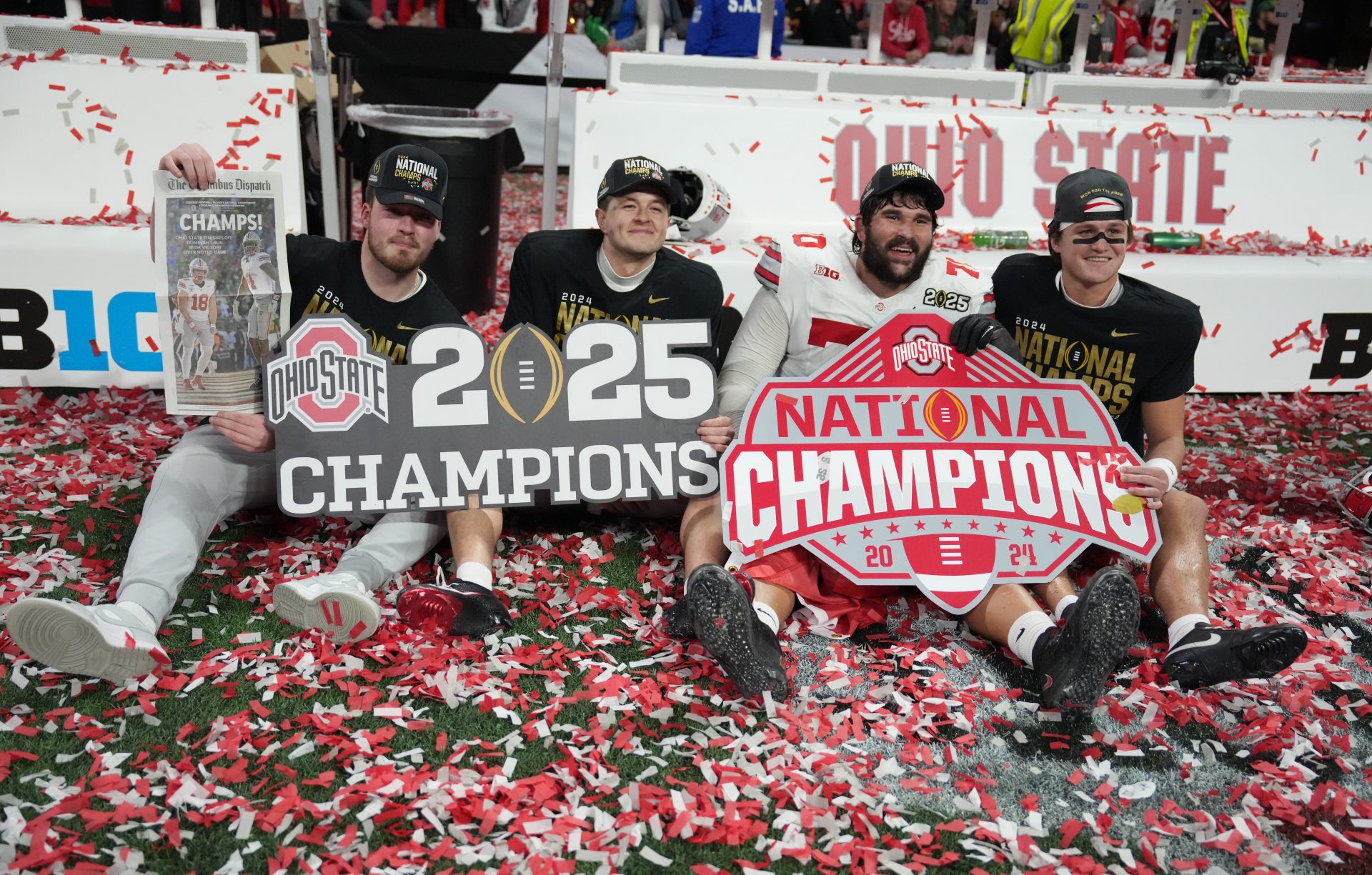 Ohio State Buckeyes players pose with signage and a commemorative newspaper after defeating the Notre Dame Fighting Irish in the CFP National Championship college football game at Mercedes-Benz Stadium.