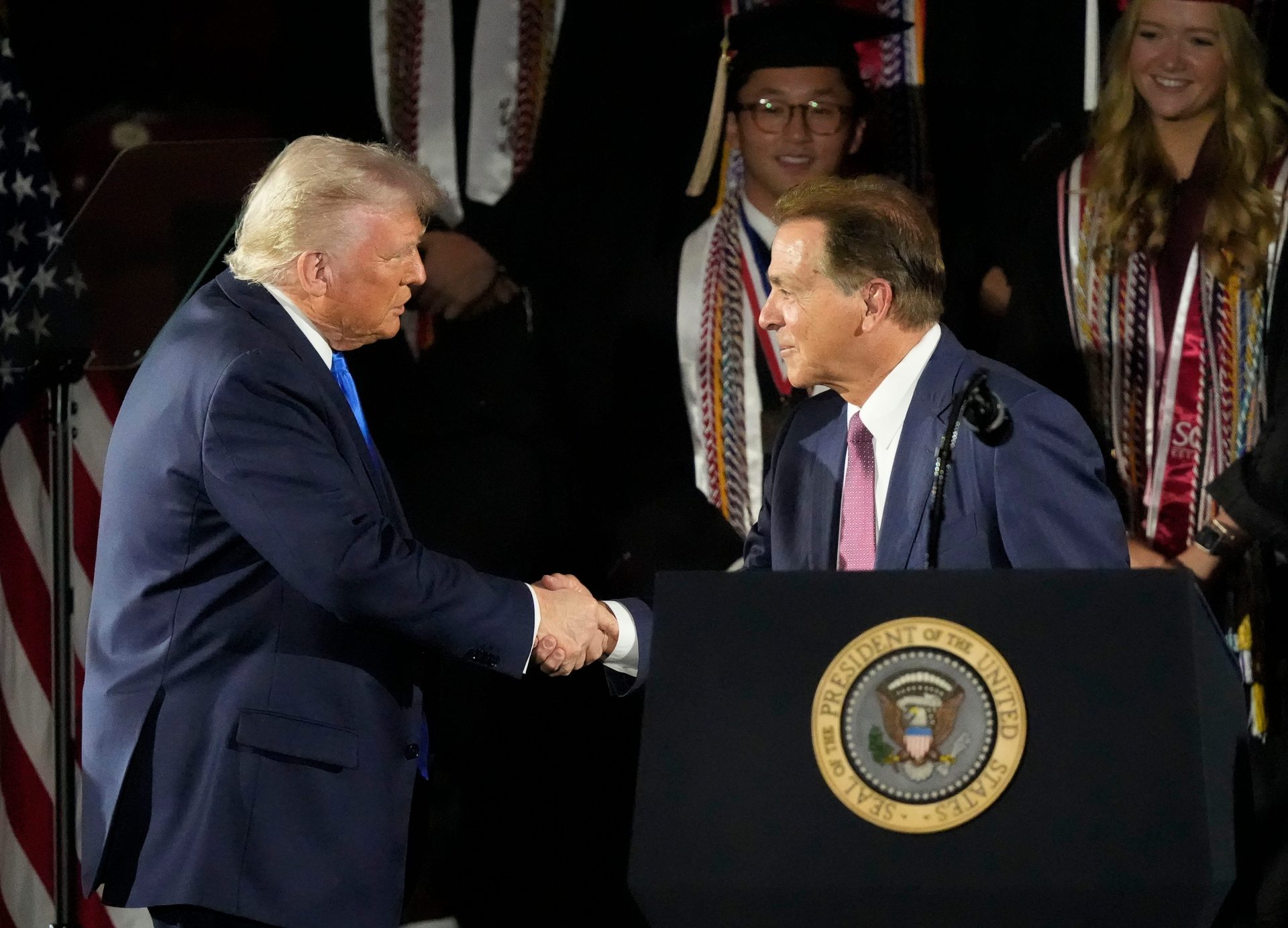 President Donald Trump shakes hands with legendary Alabama football coach Nick Saban before delivering a special commencement address to University of Alabama graduates