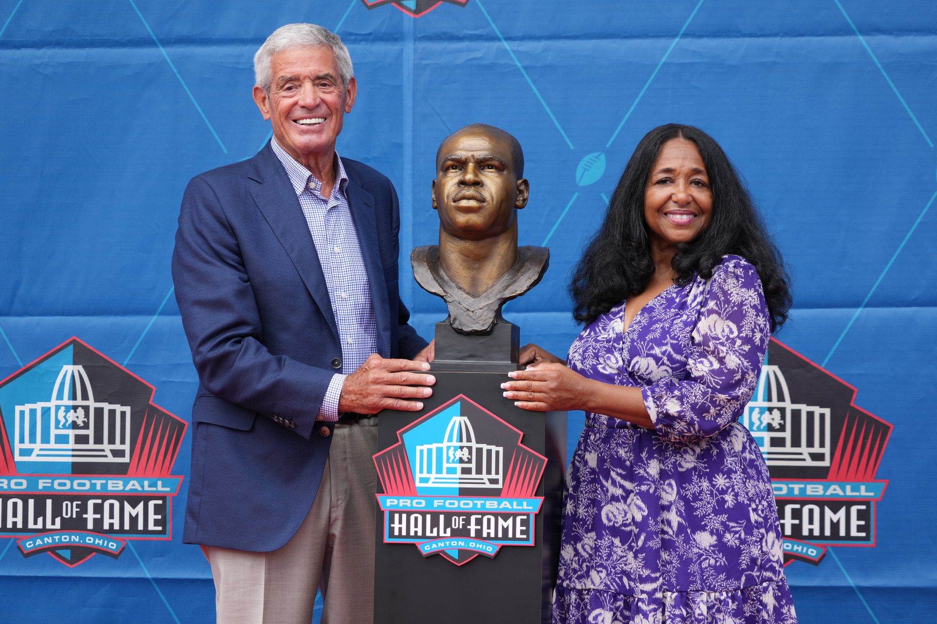 Jim Mora, left, and Melanie Mills, wife of Sam Mills poses with the bust of her late husband at his enshrinement during the Pro Football Hall of Fame Class of 2022 enshrinement  ceremony at Tom Benson Hall of Fame Stadium.