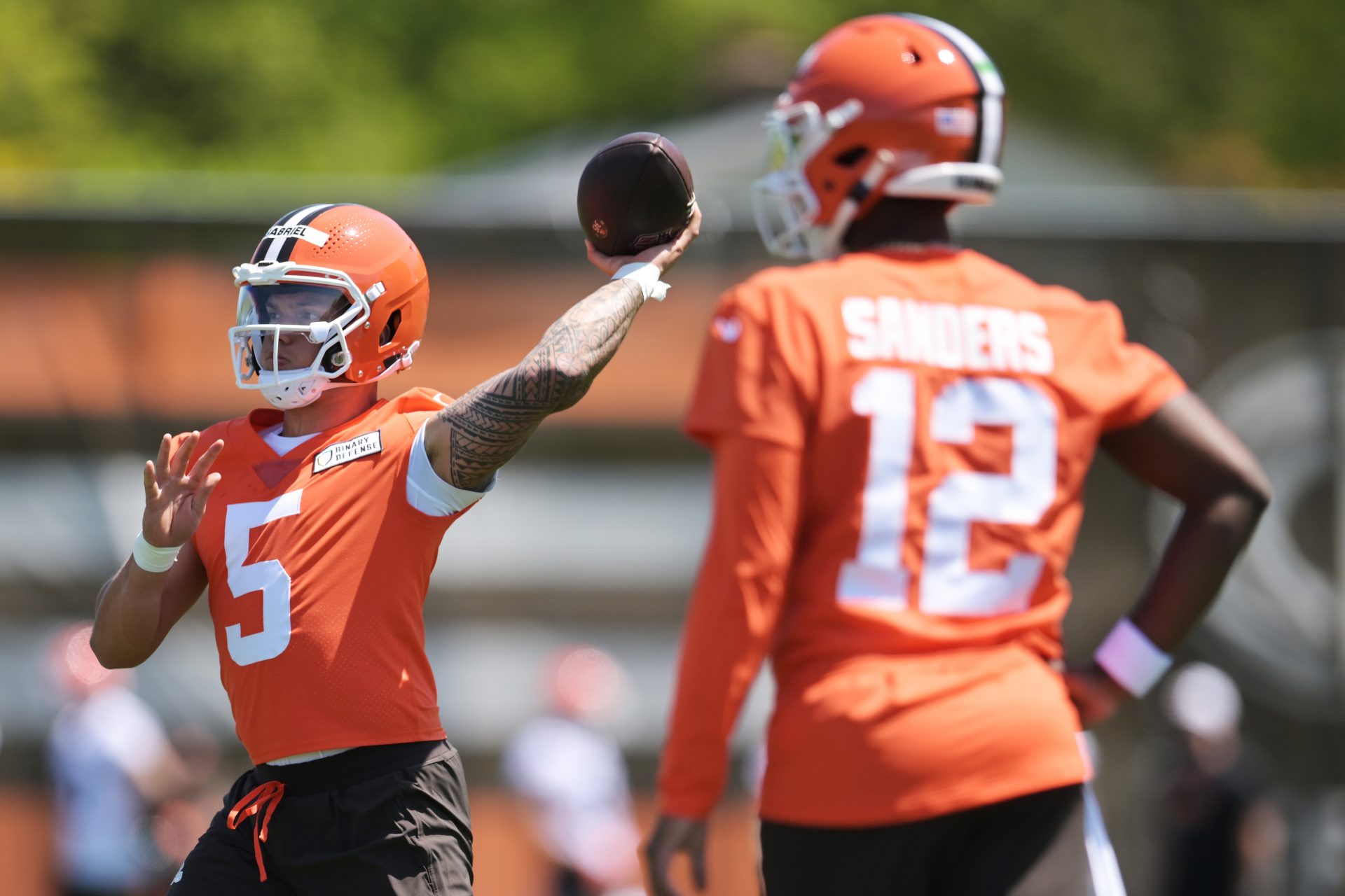 Cleveland Browns quarterback Dillon Gabriel (5) passes as quarterback Shedeur Sanders (12) looks on during rookie minicamp at CrossCountry Mortgage Campus.