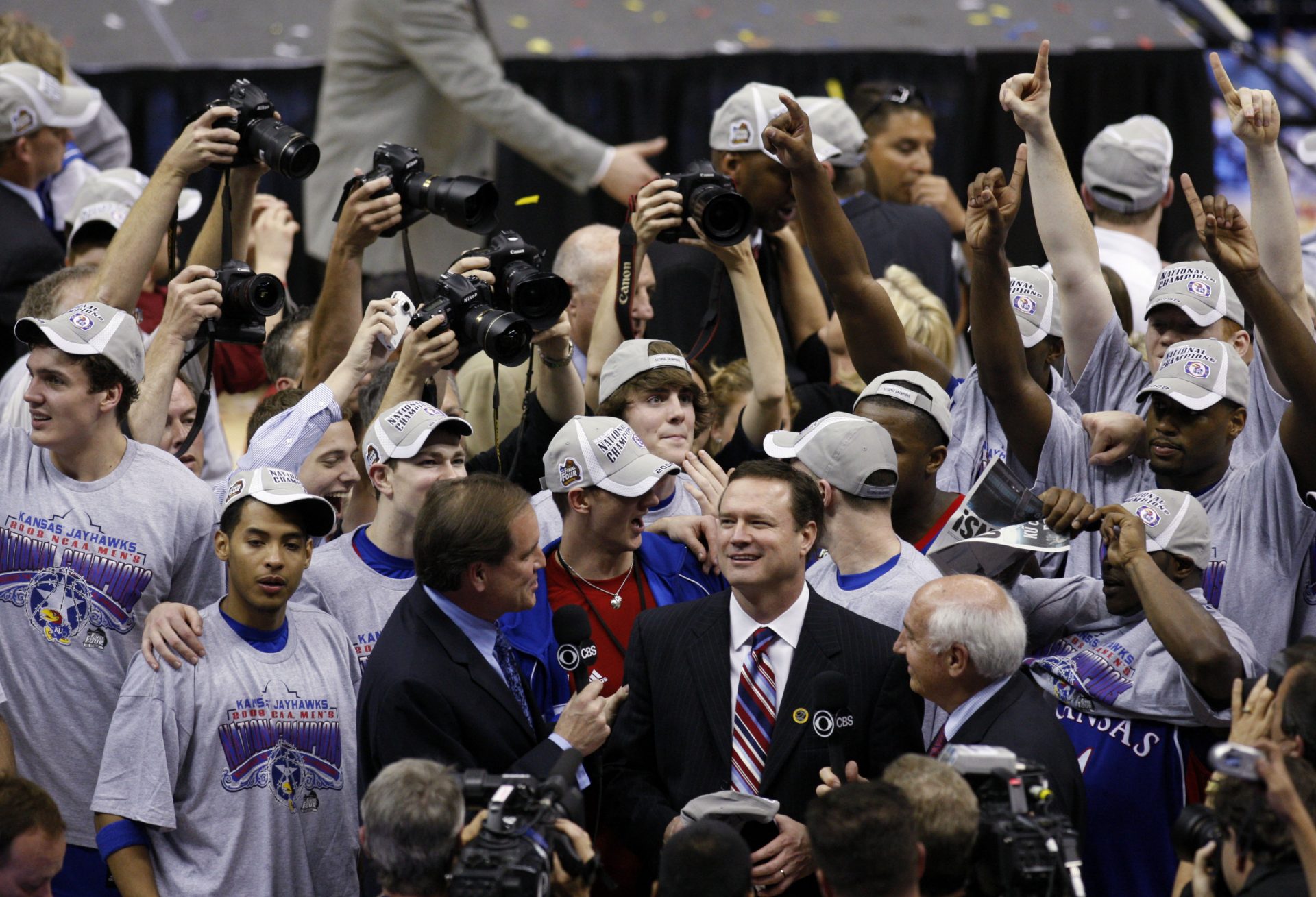 Members of the Kansas Jayhawks celebrate while head coach Bill Self is interviewed by broadcasters after defeating the Memphis Tigers in the finals of the 2008 NCAA Mens Final Four Championship at the Alamodome.  Kansas defeated Memphis 75-68 in overtime to win the national championship.