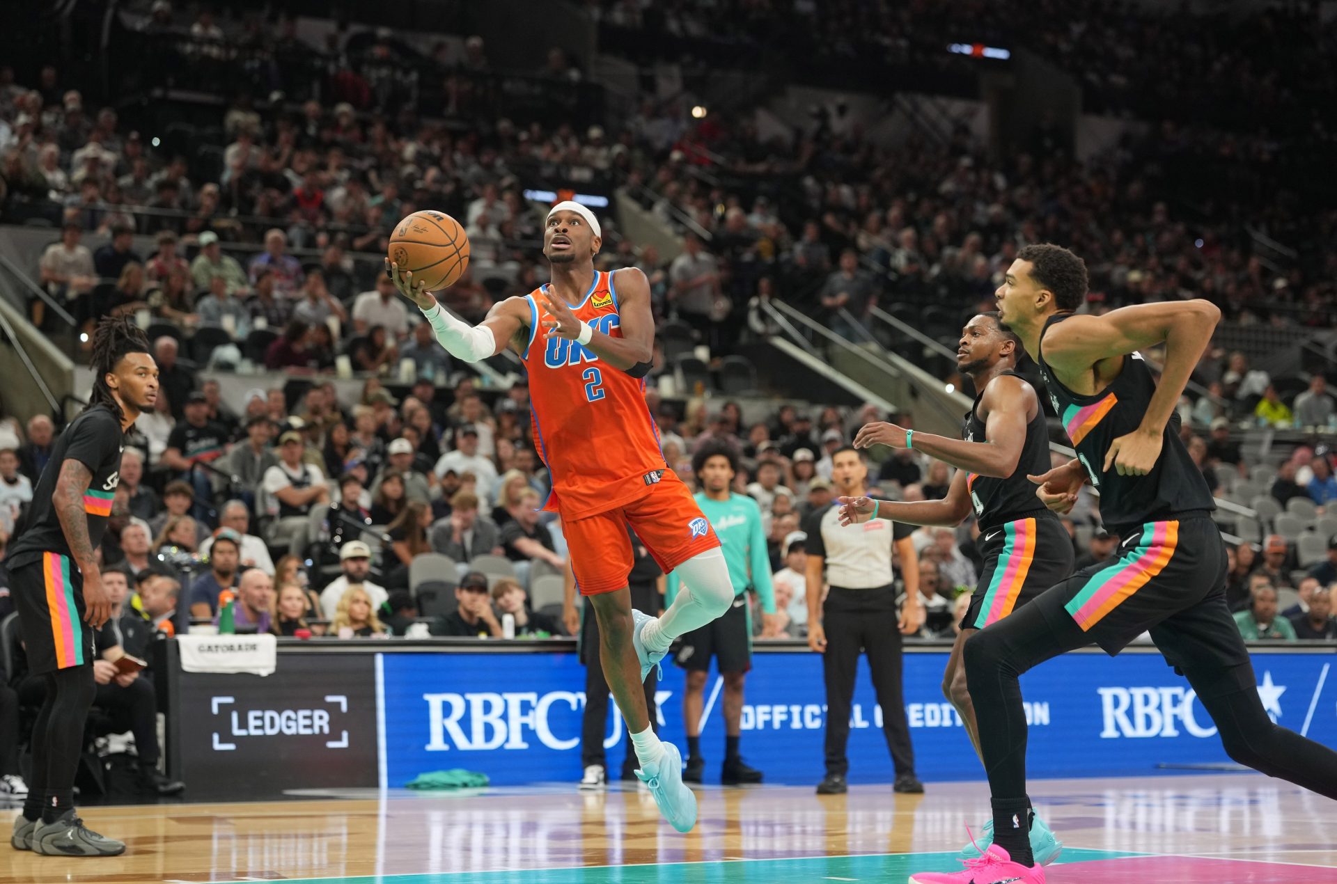 Oklahoma City Thunder guard Shai Gilgeous-Alexander (2) drives to the basket between San Antonio Spurs forward Victor Wembanyama (1) and guard Stephon Castle (5) during the second half at Frost Bank Center.
