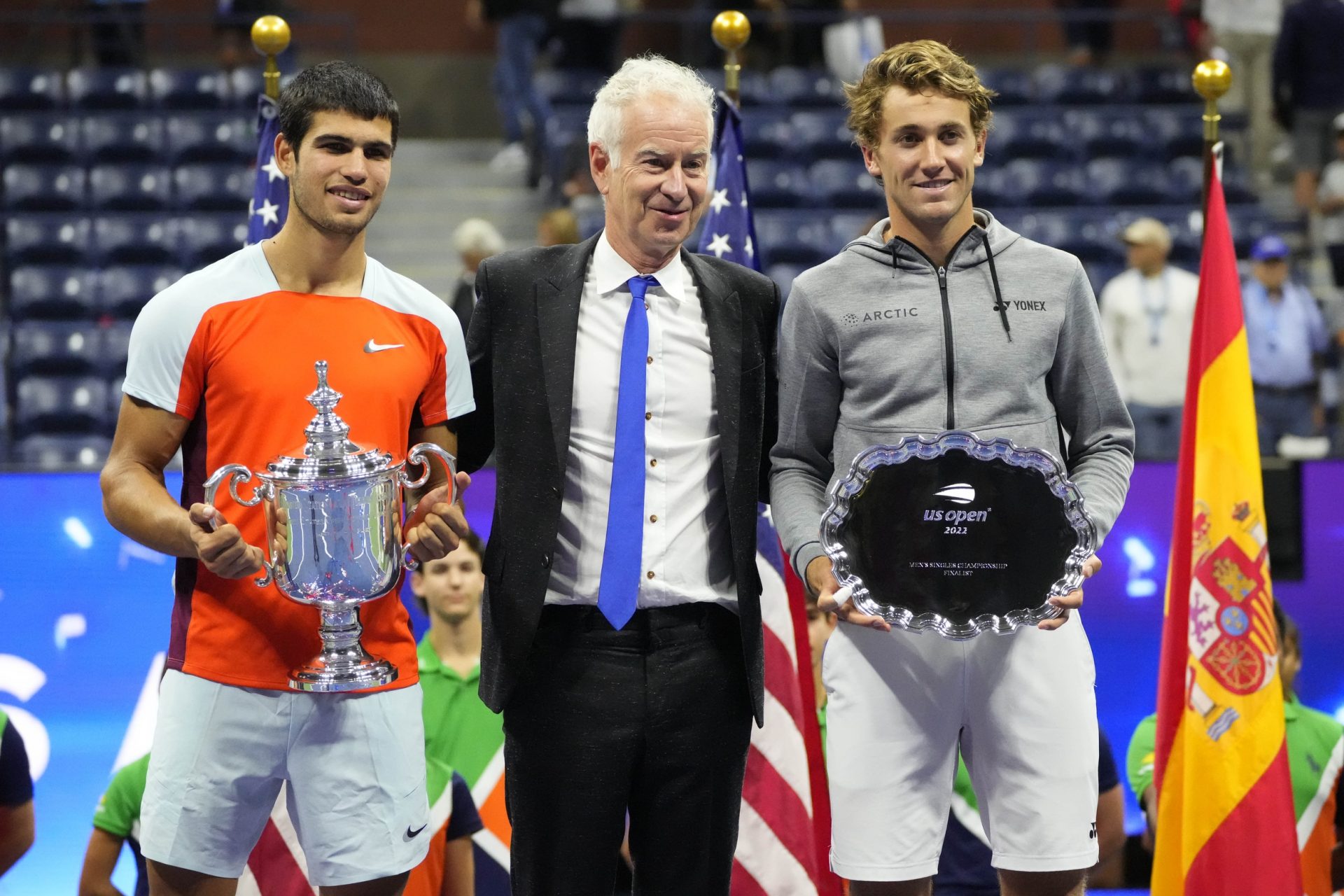 Carlos Alcaraz (ESP) (L) and Casper Ruud (NOR) (R) hold the championship and finalist trophies (respectively) while posing for a picture with International Tennis Hall of Fame member John McEnroe (M) after their match in the men's singles final on day fourteen of the 2022 U.S. Open tennis tournament at USTA Billie Jean King Tennis Center.
