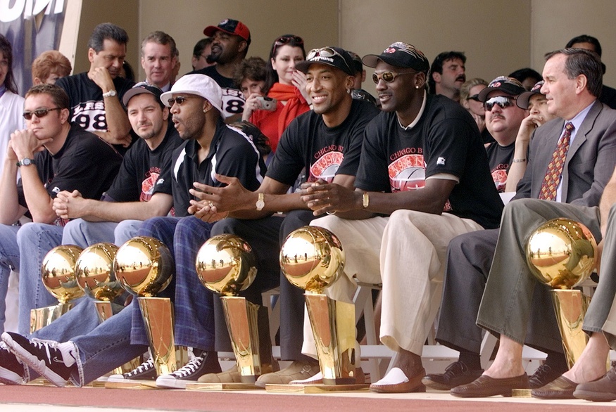 Chicago Bulls with their six championship trophies. Left to right in the front row are Luc Longley, Toni Kukoc, Ron Harper, Dennis Rodman (leaning back), Scottie Pippen, Michael Jordan and Chicago Mayor Richard Daley at a championship rally at Grant Park in Chicago.