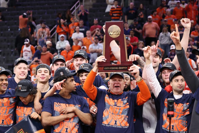 Illinois Fighting Illini head coach Brad Underwood and players celebrate with the trophy on the podium after defeating the Iowa Hawkeyes in an Elite Eight game of the South Regional of the men's 2026 NCAA Tournament at Toyota Center. Source: Troy Taormina-Imagn Images