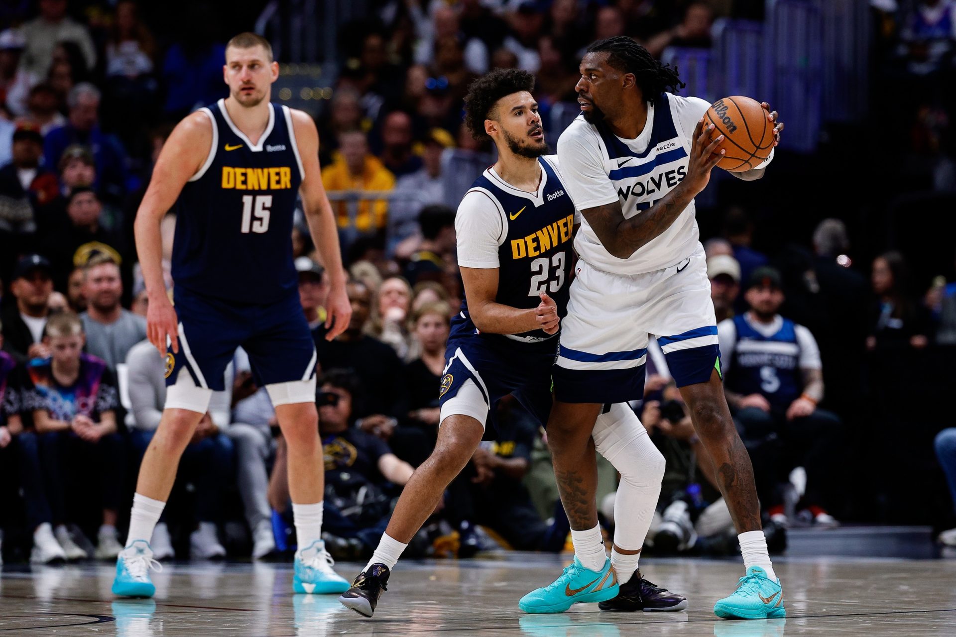 Minnesota Timberwolves center Naz Reid (11) controls the ball under pressure from Denver Nuggets forward Cameron Johnson (23) as center Nikola Jokic (15) defends in the fourth quarter during game five of the first round of the 2026 NBA Playoffs at Ball Arena - Source: Imagn Images