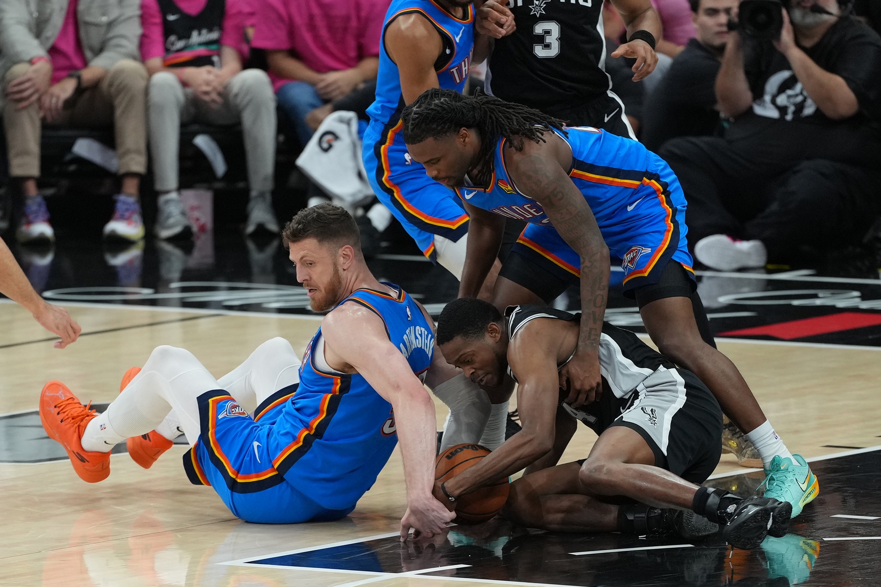 Oklahoma City Thunder guard Cason Wallace (22) and center Isaiah Hartenstein (55) attempt to get a loose ball with San Antonio Spurs guard De'aaron Fox (4) in the first half during game three of the western conference finals for the 2026 NBA playoffs at Frost Bank Center.