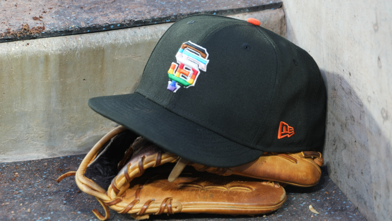 A rainbow colored San Francisco Giants logo cap and a glove in the dugout - Image Source: Imagn Images